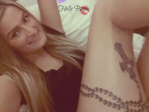 Holly Banks liegt auf dem Bett und zeigt ihr Tattoo am Bein